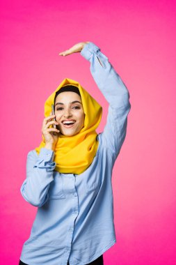Sarı tesettürlü müslüman kadın telefon teknolojisi pembe arka planda konuşuyor.