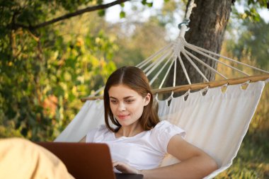 Kadınlar dışarıda bir hamakta dizüstü bilgisayarlı internetle yatıyor.