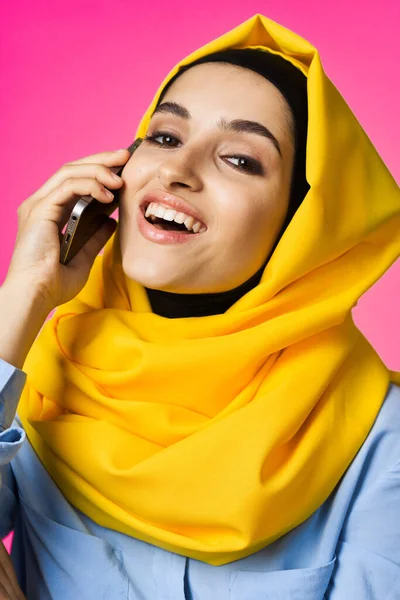 黄色のヒジャーブのイスラム教徒の女性が電話技術のピンクの背景で話しています — ストック写真