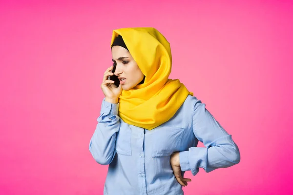 Femme musulmane en hijab jaune parlant sur le téléphone technologie fond rose — Photo