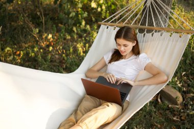 Kadınlar hamakta dizüstü bilgisayarlı tatil internetleriyle yatıyor.