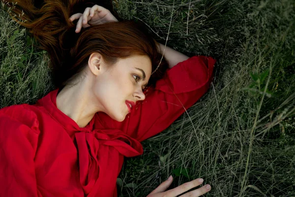 Pretty woman in red dress lies on the grass sun summer nature — Stock Photo, Image