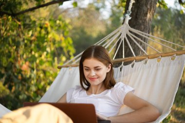 Doğada bir hamakta dizüstü bilgisayarın önünde çalışan bir kadın.