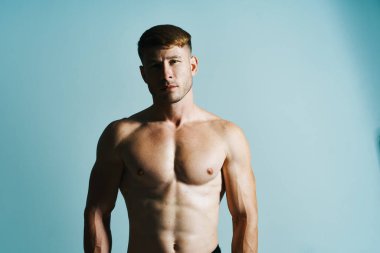 Kaslı vücutlu vücut geliştirici mavi arka plana basar