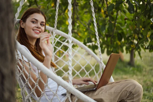 Bilgisayarlı kadın dışarıda hamakta dinleniyor.