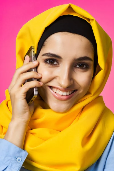 Mujer musulmana en hijab amarillo hablando sobre la tecnología del teléfono de fondo rosa —  Fotos de Stock