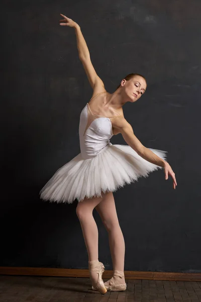 Mulher bailarina em um branco tutu dança posando desempenho fundo escuro — Fotografia de Stock