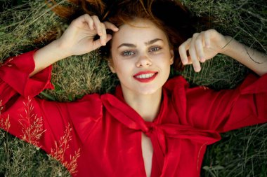 Kırmızı elbiseli kadın çimenlerin üzerinde uzanmış özgürlüğe bakıyor.