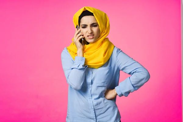 Muslimische Frau im gelben Hijab telefoniert mit rosa Technologie-Hintergrund — Stockfoto
