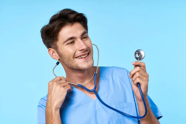 Homem em tratamento de saúde uniforme médico estetoscópio exame azul fundo — Fotografia de Stock