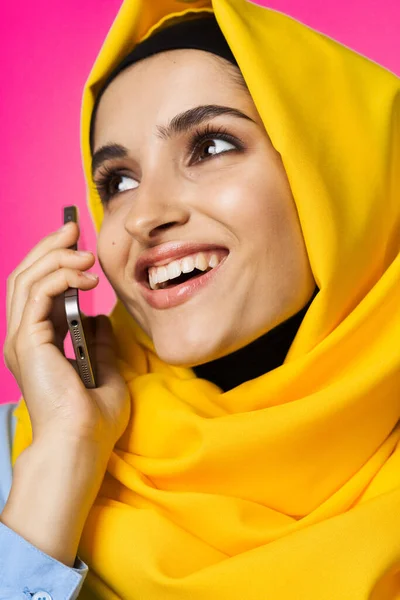 Mujer musulmana en hijab amarillo hablando sobre la tecnología del teléfono de fondo rosa —  Fotos de Stock