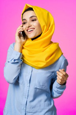 Sarı tesettürlü müslüman kadın telefonda pembe teknolojiyle konuşuyor.