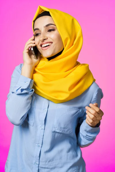 Musulmana mujer en amarillo hijab hablando en el teléfono rosa tecnología fondo —  Fotos de Stock