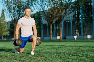 Atletik adam sabah halterlerle antrenman yapıyor. Park.