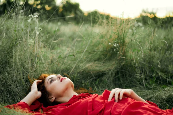 Pretty woman in red dress lies on the grass freedom landscape — Stock Photo, Image