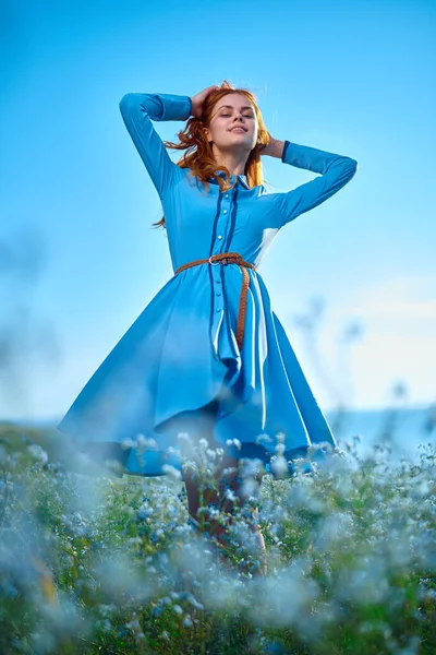 Mavi elbiseli bir kadın doğa çiçekli bir tarlada yürüyor.