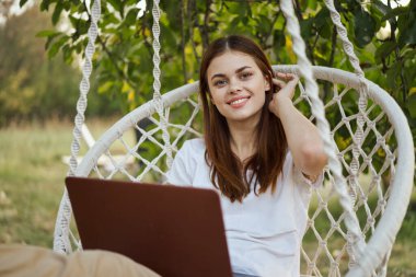 Hamakta dizüstü bilgisayarı dinlenen neşeli bir kadın.