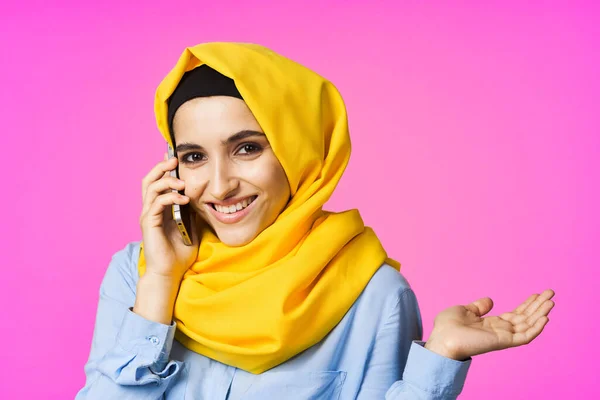 Musulmana mujer en amarillo hijab hablando en el teléfono rosa tecnología fondo —  Fotos de Stock