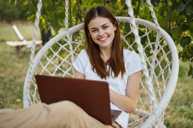 Hamakta dizüstü bilgisayarı dinlenen neşeli bir kadın.