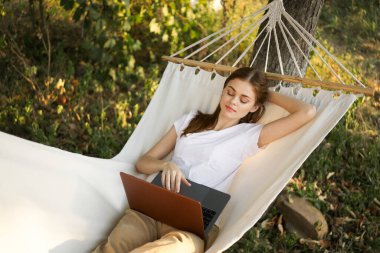 Kadınlar hamakta dizüstü bilgisayarlı tatil internetleriyle yatıyor.