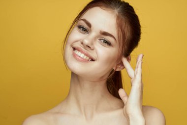 Çıplak omuzlu, beyaz tenli, sarı arkaplan pozu veren bir kadın.