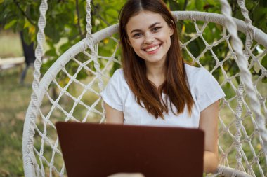 Hamakta dizüstü bilgisayarı dinlenen neşeli bir kadın.