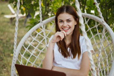 Hamakta dizüstü bilgisayarı dinlenen neşeli bir kadın.