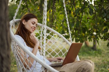 Bilgisayarlı kadın dışarıda hamakta dinleniyor.