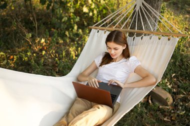 Kadınlar hamakta dizüstü bilgisayarlı tatil internetleriyle yatıyor.