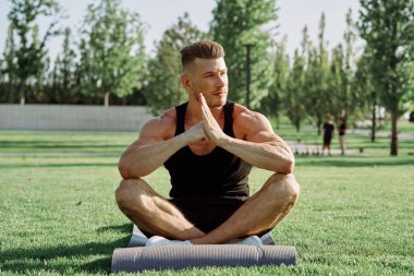 Sportif adam parkta çimlerde oturuyor.