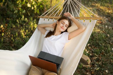 Kadınlar hamakta dizüstü bilgisayarlı tatil internetleriyle yatıyor.