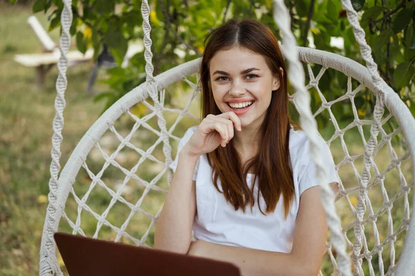 Hamakta dizüstü bilgisayarı dinlenen neşeli bir kadın.