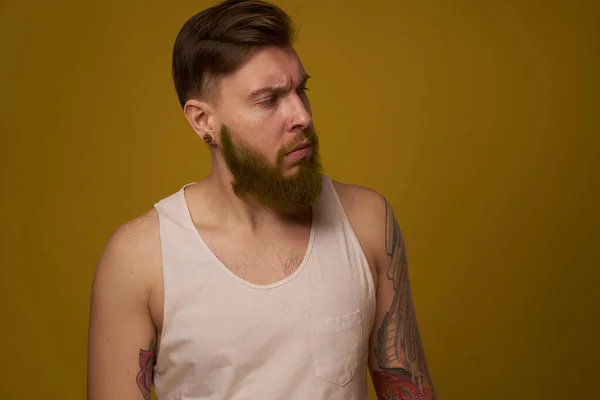 Hombre barbudo en camiseta blanca con tatuajes en sus brazos posando mirada seria — Foto de Stock