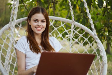 Hamakta dizüstü bilgisayar teknolojisiyle gülümseyen kadın.