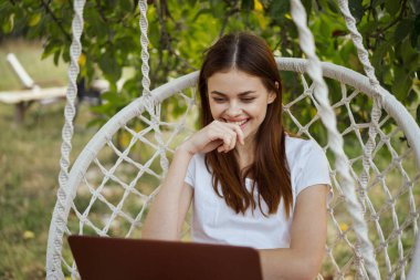 Hamakta dizüstü bilgisayarı dinlenen neşeli bir kadın.