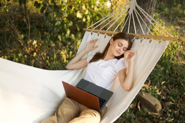 Kadınlar hamakta dizüstü bilgisayarlı tatil internetleriyle yatıyor.