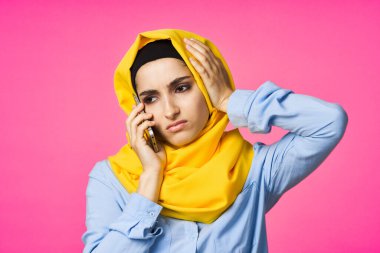 Sarı tesettürlü müslüman kadın telefon teknolojisi pembe arka planda konuşuyor.