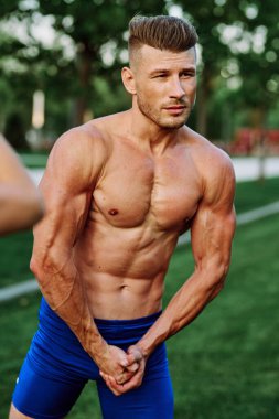 Şişirilmiş kaslı vücutlu bir adam dışarıda sağlık egzersizi yapıyor.