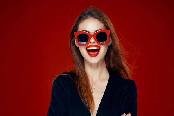 Hezká žena nosí sluneční brýle módní představovat účes červené pozadí — Stock fotografie