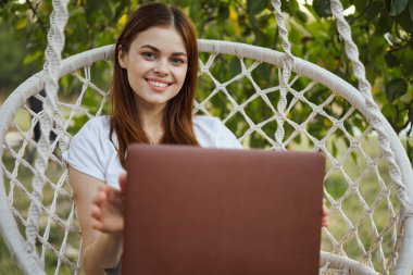 Hamakta dizüstü bilgisayar teknolojisiyle gülümseyen kadın.