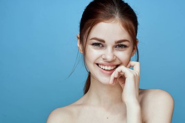 Çıplak omuzlu, at kuyruklu, mavi arka plan pozu veren bir kadın.