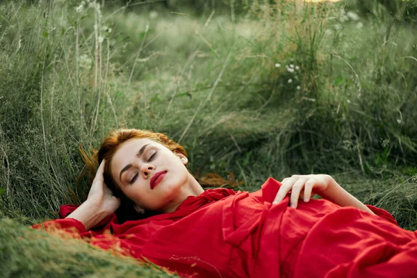 Pretty woman in red dress lies on the grass freedom landscape — Stock Photo, Image