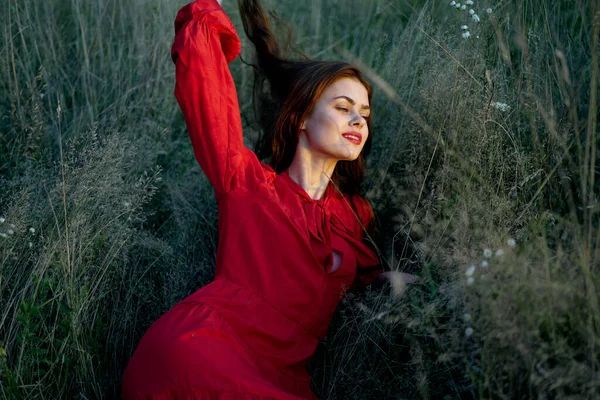 Pretty woman in red dress lies on the grass nature sun — Stock Photo, Image