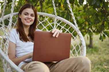 Hamakta dizüstü bilgisayar teknolojisiyle gülümseyen kadın.