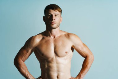 Kaslı vücutlu vücut geliştirici mavi arka plana basar