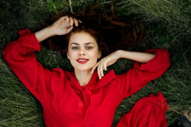 Kırmızı elbiseli kadın çimenlerin üzerinde uzanmış özgürlüğe bakıyor.