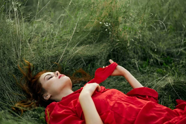 Hübsche Frau in rotem Kleid liegt auf dem Gras in der Natur frische Luft — Stockfoto