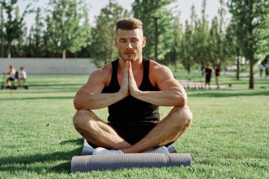 Sportif adam parkta çimlerde oturuyor.