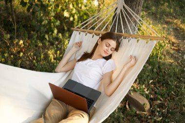 Kadınlar hamakta dizüstü bilgisayarlı tatil internetleriyle yatıyor.