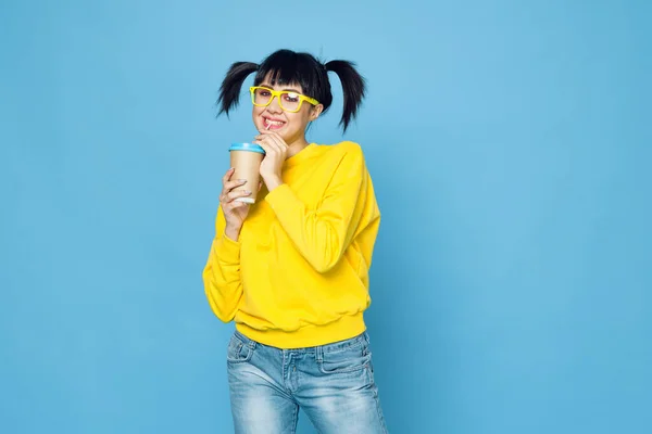 Vidám nő copfos sárga pulóverben ital kék háttér — Stock Fotó